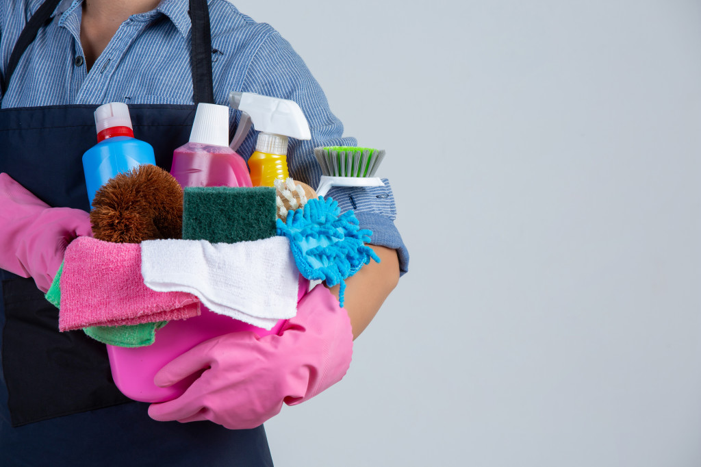 Young girl is holding cleaning product, gloves and rags in the b