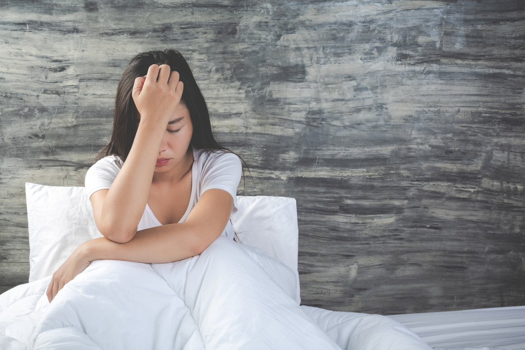 The girl is depressed on a white bed and has a gray cement wall