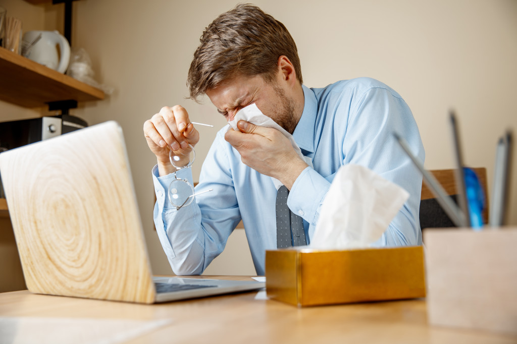 Sick man while working in office, businessman caught cold, seasonal flu.