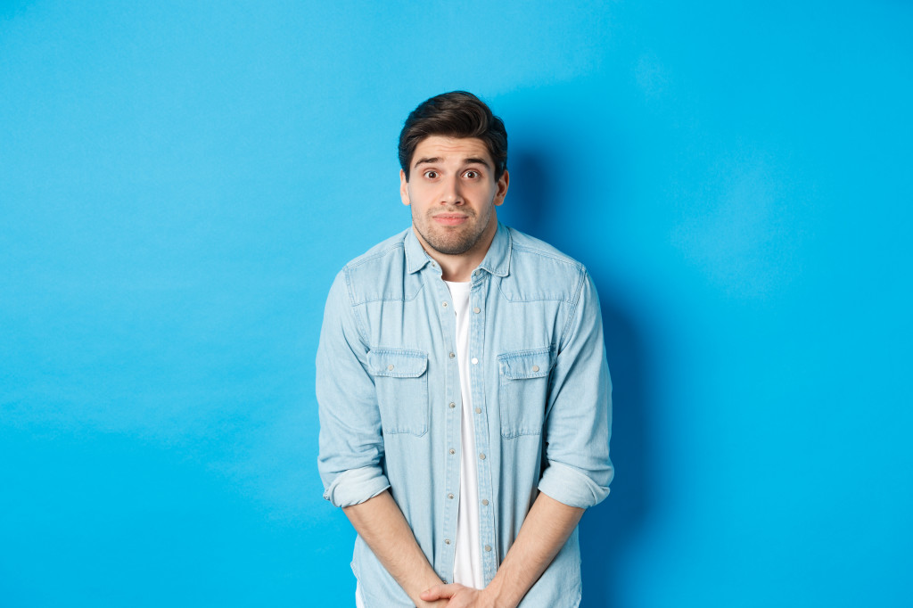 Embarrassed guy want to pee, waiting in line for toilet, standing against blue background