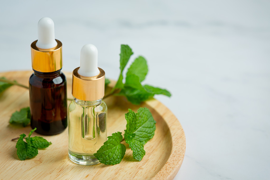 Essential oil of peppermint in bottle with fresh green peppermin