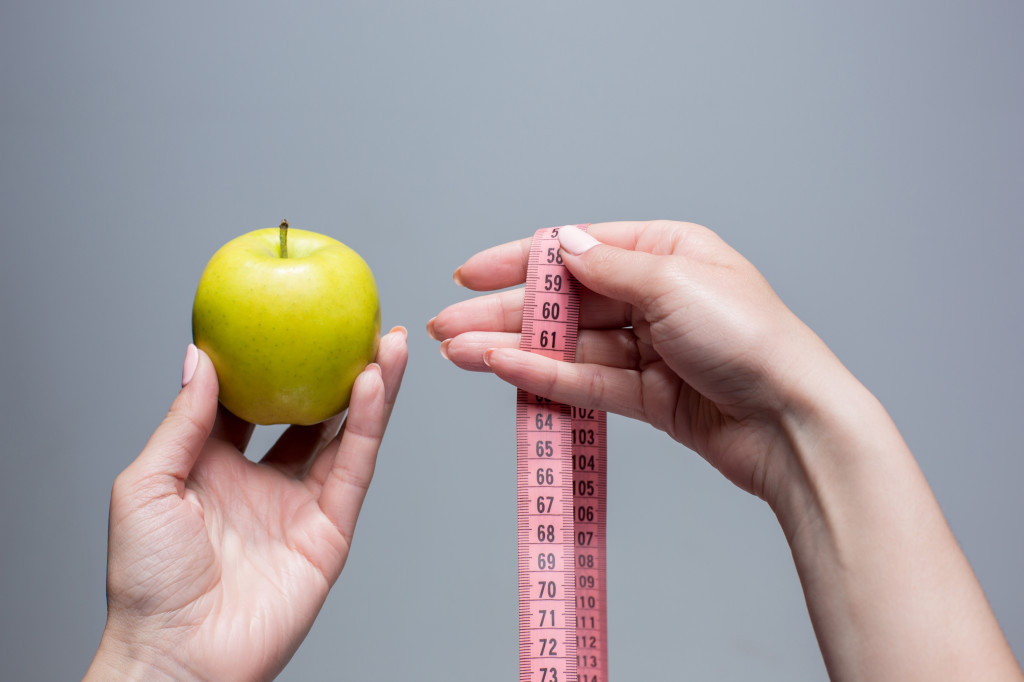 Green apple in female hands on gray background. Weight loss, diet