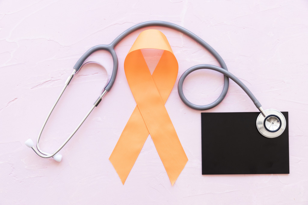 an-orange-awareness-ribbons-with-stethoscope-over-slate-on-pink-background