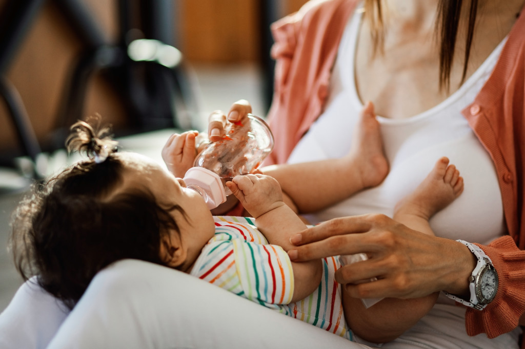 Baby girl drinking water while relaxing in mother's lap.